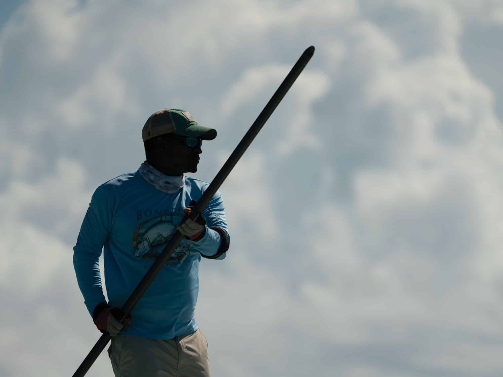 a man standing on flats boat platform uses pole to push through